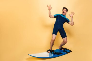 Korkmuş genç bir adam portresi tam uzunlukta sarı arka plan üzerinde izole bir tahta üzerinde sörf mayo giymiş