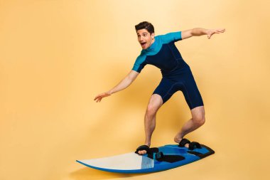 Heyecanlı bir genç adam portresi tam uzunlukta sarı arka plan üzerinde izole bir tahta üzerinde sörf mayo giymiş