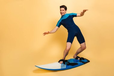 Genç gülümseyen bir adam portresi tam uzunlukta sarı arka plan üzerinde izole bir tahta üzerinde sörf mayo giymiş