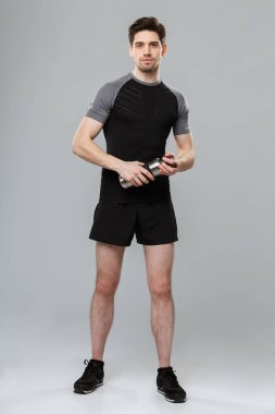 Görüntü üzerine gri duvar arka plan holding şişe su ile izole ayakta yakışıklı genç sporcu.