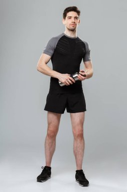 Görüntü üzerine gri duvar arka plan holding şişe su ile izole ayakta yakışıklı genç sporcu.