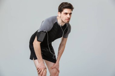 Konsantre bir genç sporcu istirahat izole gri arka plan üzerinde iken kulaklık ile müzik dinlemek portresi