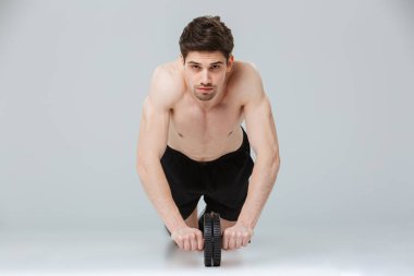 İtme yaparken konsantre genç yarı çıplak sporcu portresi ups ile gri arka plan üzerinde izole bir ekipman