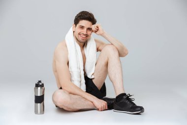 Havlu ve su şişe gri arka plan üzerinde izole otururken dinlenme bir neşeli genç yarı çıplak sporcu portresi