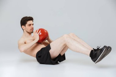 Gri arka plan üzerinde izole bir ağır top ile abs egzersizleri yapıyor bir konsantre genç yarı çıplak sporcu portresi