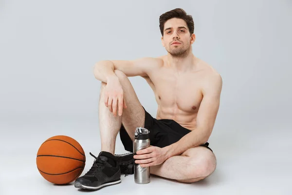 Портрет Уверенного Молодого Полуобнаженного Спортсмена Держащего Бутылку Воды Сидя Баскетболом — стоковое фото