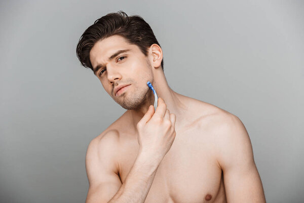 Beauty portrait of half naked charming young man shaving isolated over gray background