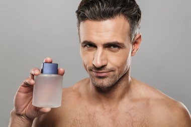 Yakışıklı olgun neşeli adam parfüm tutan çıplak gri duvar arka plan üzerinde izole ayakta, fotoğraf.