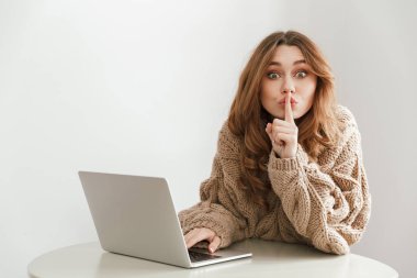 Görüntü kafede masada oturan ve dizüstü bilgisayar kullanırken dudaklarında parmak koyarak ciddi kadın 20'li yaşlarda giyen örme kazak