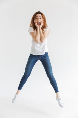 Tam boy görüntü Surprised yanakları süre atlama ve gri arka plan üzerinde kameraya bakarak tutan t-shirt içinde çığlık atan kadın