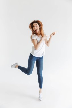 Tam boy görüntü arka plan gri uzağa işaret ve kameraya bakmaktan ederken t-shirt atlama içinde gidiş mutlu kadın