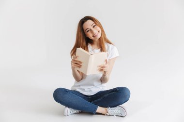 Bacaklar ile otururken kitap tutan mutlu bir genç kız portresi izole beyaz arka plan üzerinde çarpı işareti