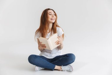 Bacaklar ile otururken kitap tutan bir gülümseyen kız portresi izole beyaz arka plan üzerinde çarpı işareti