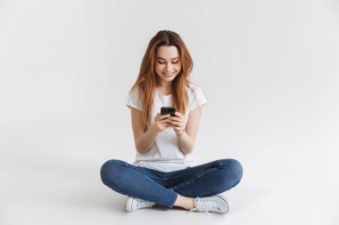 Bacaklar ile otururken cep telefonuyla mutlu bir genç kız portresi izole beyaz arka plan üzerinde çarpı işareti