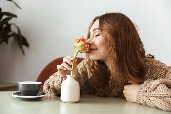 Foto Una Mujer Encantadora Sentada Mesa Cafetería Oliendo Flor Mientras — Foto de Stock