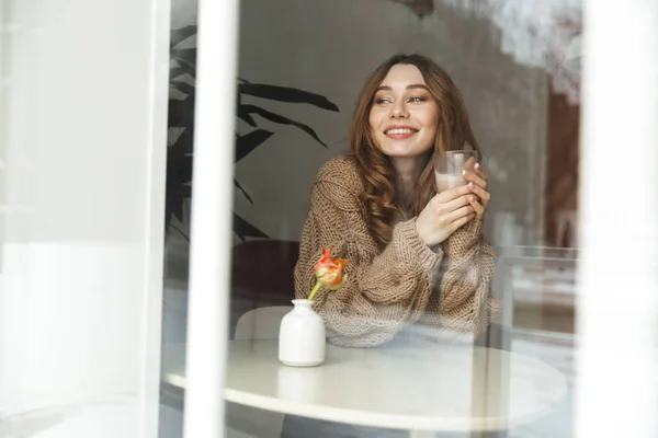 Úsměvem Mladá Žena Svetru Drží Šálek Kávy Při Sezení Stolu — Stock fotografie