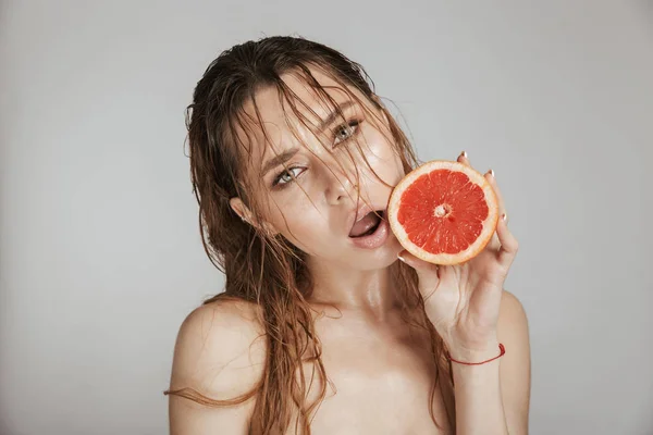 时尚肖像的裸体漂亮的女人与化妆和湿头发举行切片柚子隔离在灰色背景下 — 图库照片