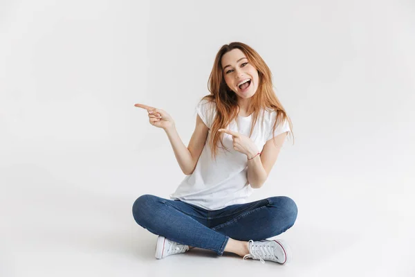 Gelukkige Vrouw Shirt Zittend Vloer Weg Wijzen Terwijl Camera Kijkt — Stockfoto