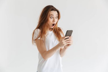 Şok kadında rahat kıyafetler mesaj smartphone üzerinde gri arka plan üzerinde yazma.