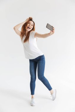 Tam boy görüntü selfie saç gri arka plan üzerinde dokunmadan süre Smartphone'da yapma rahat kıyafetler içinde oynak kadın