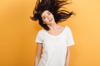 Saç sallayarak kamera seyir sarı arka plan üzerinde izole duran genç mutlu kadın fotoğrafı.