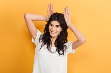 Güzel genç bayan eğleniyor kamera seyir sarı arka plan üzerinde izole ayakta görüntüsünü.