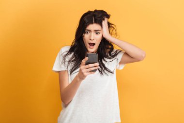 Cep telefonuyla bir yana sohbet arıyorsunuz sarı arka plan üzerinde izole duran korkmuş şok genç güzel kadın görüntüsünü.