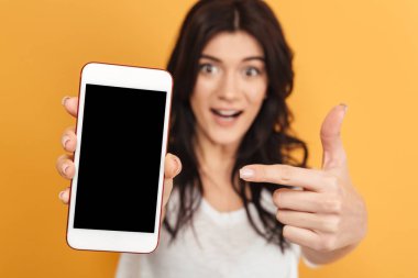 Görüntü izole kamera gösteren ekran cep telefonu görünümlü sarı arka plan üzerinde duran genç güzel kadın.