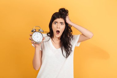 Genç şok heyecanlı kadın çalar saat kamera seyir tutan sarı arka plan üzerinde izole görüntüsünü.
