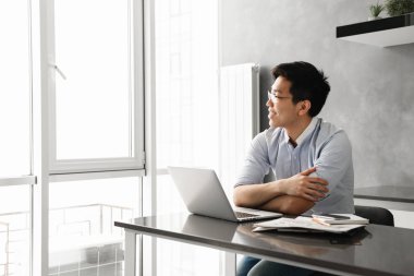 Evrak işlerini evde masada otururken dizüstü bilgisayar üzerinde çalışan mutlu bir genç Asyalı adam portresi