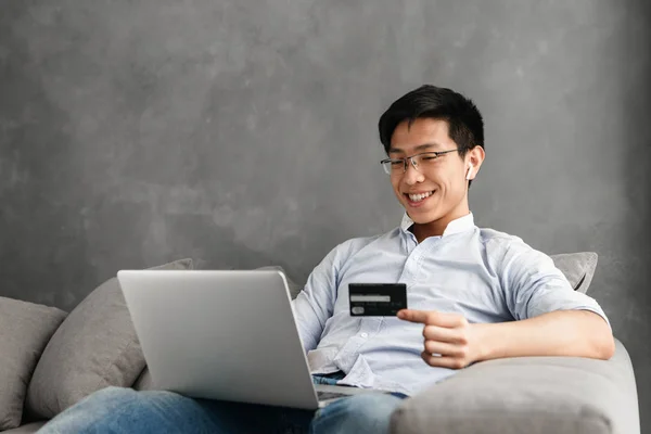 집에서 노트북 컴퓨터를 아시아 남자의 초상화 옆으로 카드를 소파에 — 스톡 사진