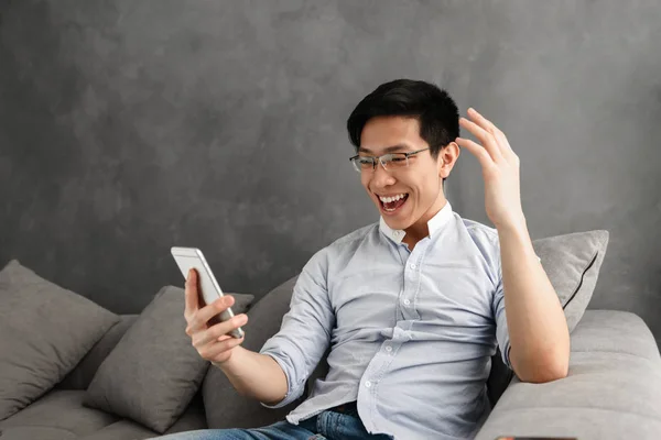 Portrait Excited Young Asian Man Using Mobile Phone While Sitting — Stock Photo, Image
