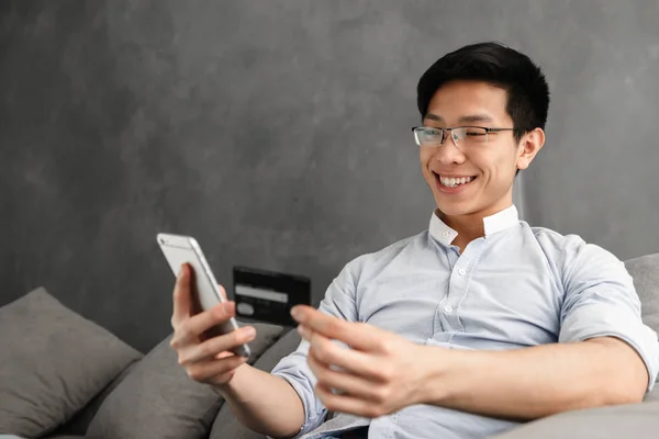 Boldog Fiatal Ázsiai Ember Használ Mozgatható Telefon Hitelkártya Míg Otthon — Stock Fotó