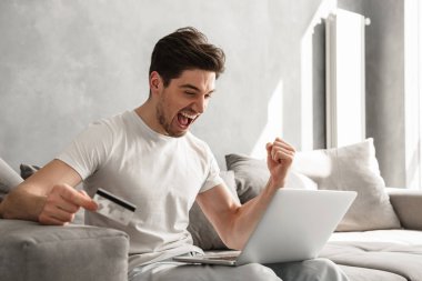 Defter ve kredi kartı online alışveriş için evde kullanırken rahat kenetlenmesi içinde memnun adam 30'lu fotoğrafı yumruklar