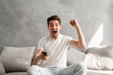 Neşeli adam 30'lu oturma odasında kanepede oturan ve yumruğunu kenetlenmesi ile Tv izlerken rahat giyim fotoğrafı