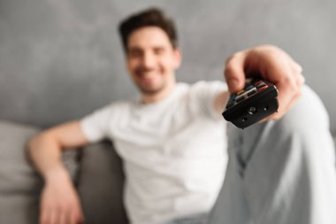 Uzaktan kumanda, Genç adam 30'lu oturma odasında kanepede oturan ve televizyon izlerken rahat t-shirt odaklı bulanık fotoğraf