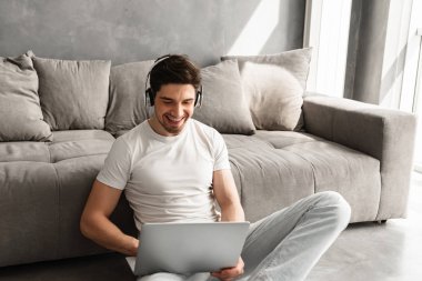 Mutlu adam kapalı ve laptop kablosuz kulaklık ile müzik dinleme katta oturan siyah saçlı