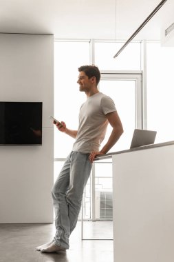 Temel giyim evde kalırken cep telefonuyla yakışıklı adamın profil fotoğrafta tam uzunlukta