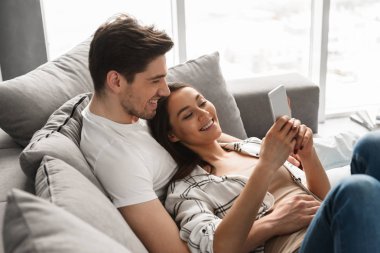 Mutlu aile portresi seven erkek ve kadın evde koltukta yalan ve istimal hareket eden telefon