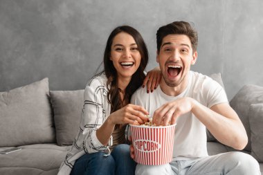 Evde kanepede oturan ve sana patlamış mısır yemek yerken bakmak genç mutlu aile görüntüsü