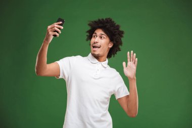 Yeşil duvar arka plan yapmak selfie cep telefonuyla izole duygusal Afrika kıvırcık delikanlı imajını.