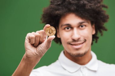 Neşeli genç Afrika kıvırcık adam bitcoin tutan yeşil duvar arka plan üzerinde izole görüntüsünü.