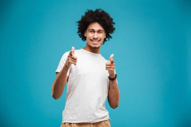Neşeli genç Afrika kıvırcık adam kamera işaret arıyorum mavi arka plan üzerinde izole ayakta görüntüsünü.