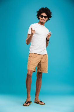 Görüntü izole kamera işaret arıyorum mavi arka plan üzerinde duran Afrika kıvırcık yakışıklı genç.