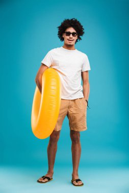 Kauçuk halka tutarak kamera arıyorum mavi arka plan üzerinde izole mutlu yakışıklı genç Afrika kıvırcık adam ayakta fotoğrafı.