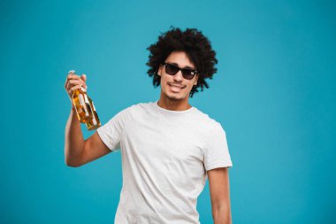 Mutlu genç Afrika kıvırcık adam bira tutan mavi arka plan üzerinde izole ayakta görüntüsünü.