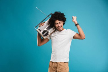 Kazanan jest yapmak imge-in duygusal genç Afrika kıvırcık adam boombox tutan mavi arka plan üzerinde izole ayakta.