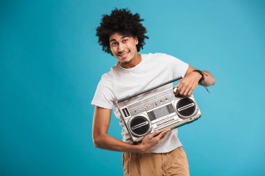 Heyecanlı genç Afrika kıvırcık adam boombox tutan mavi arka plan üzerinde izole ayakta görüntüsünü.