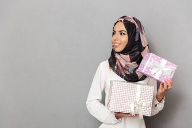 Mevcut kutularını gösteren ve gri arka plan üzerinde izole kopya alanı uzağa bakarak neşeli genç bir Arap kadın portresi