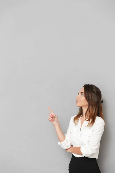 兴奋开朗的年轻企业妇女的形象站在灰色墙上的背景下 看着旁边的指针 — 图库照片